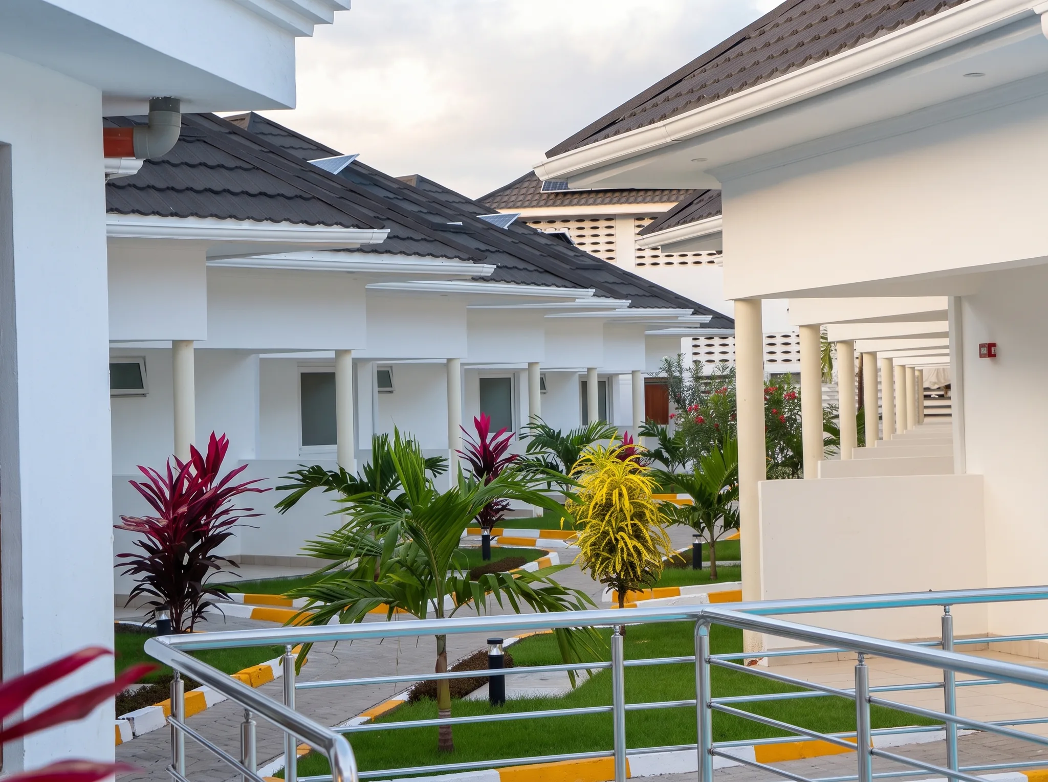 Scenic cottage villas exterior row with landscaped gardens, paved walkway and stainless steel veranda railings at Diani Darling Cottages