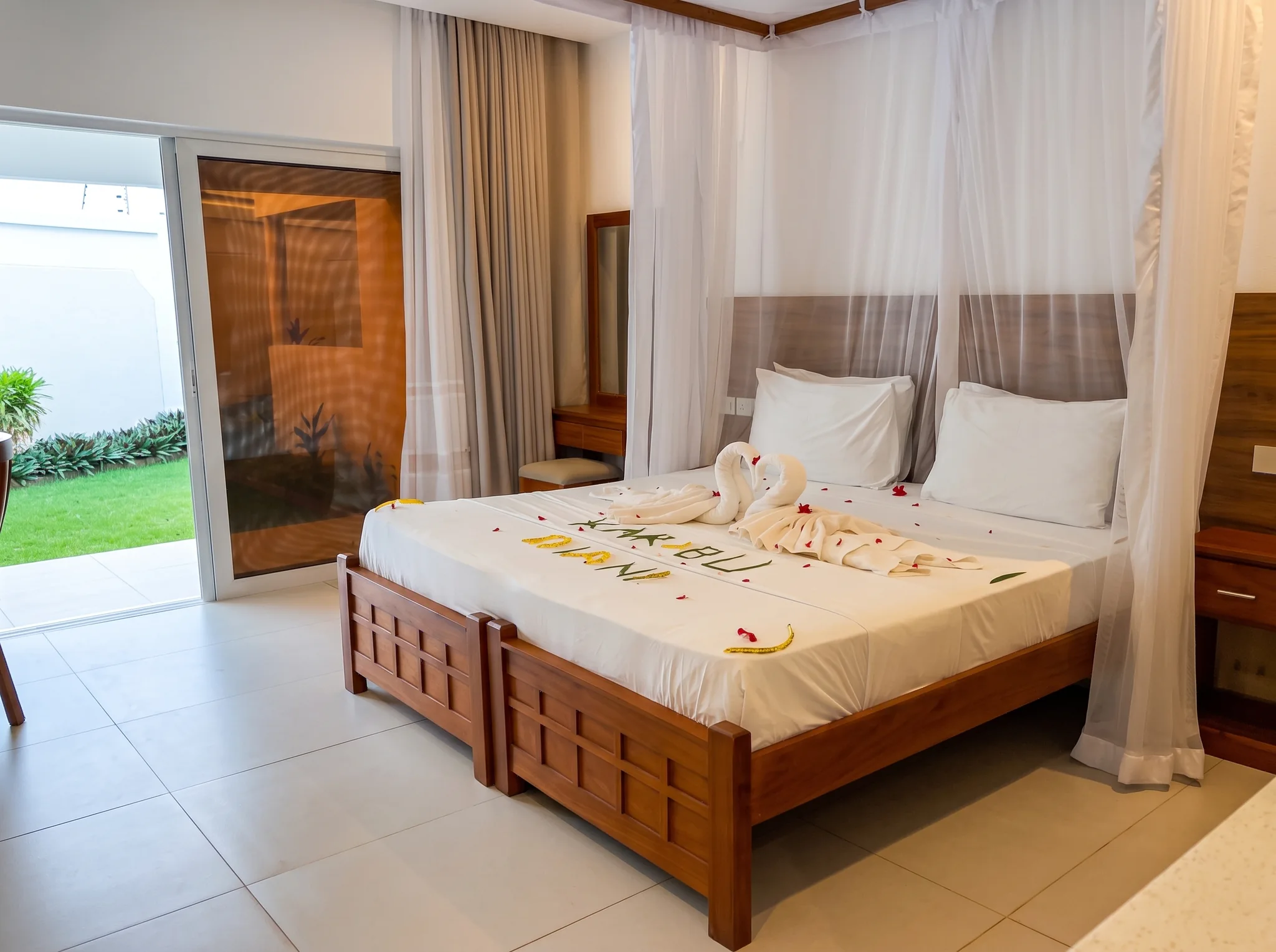 Romantic Swahili-style king bed with Karibu Diani flower petal welcome and swan towel art at Diani Darling Cottages
