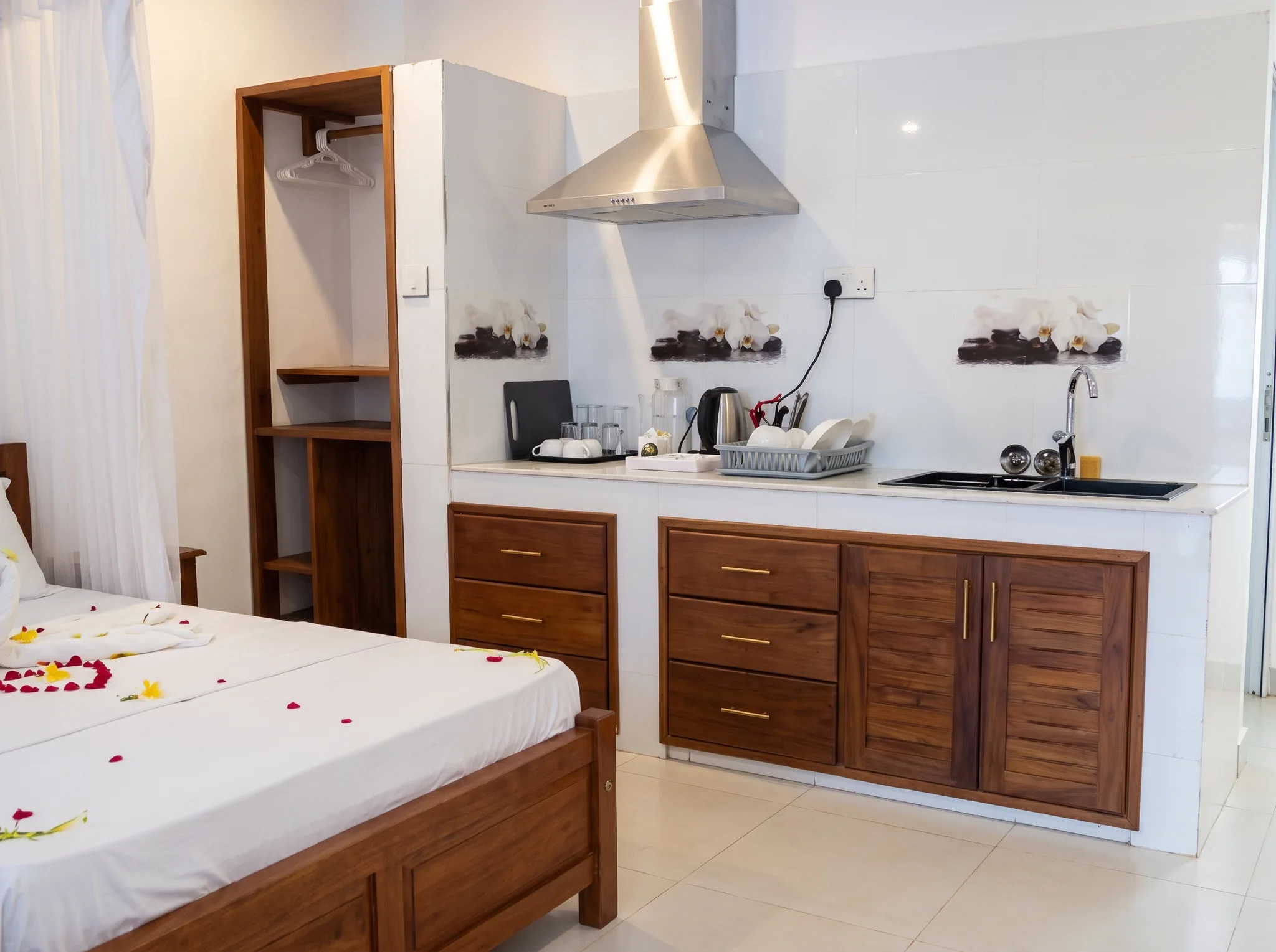 Open-plan studio layout highlighting modern kitchenette with range hood, teak cabinets, and romantic king bed