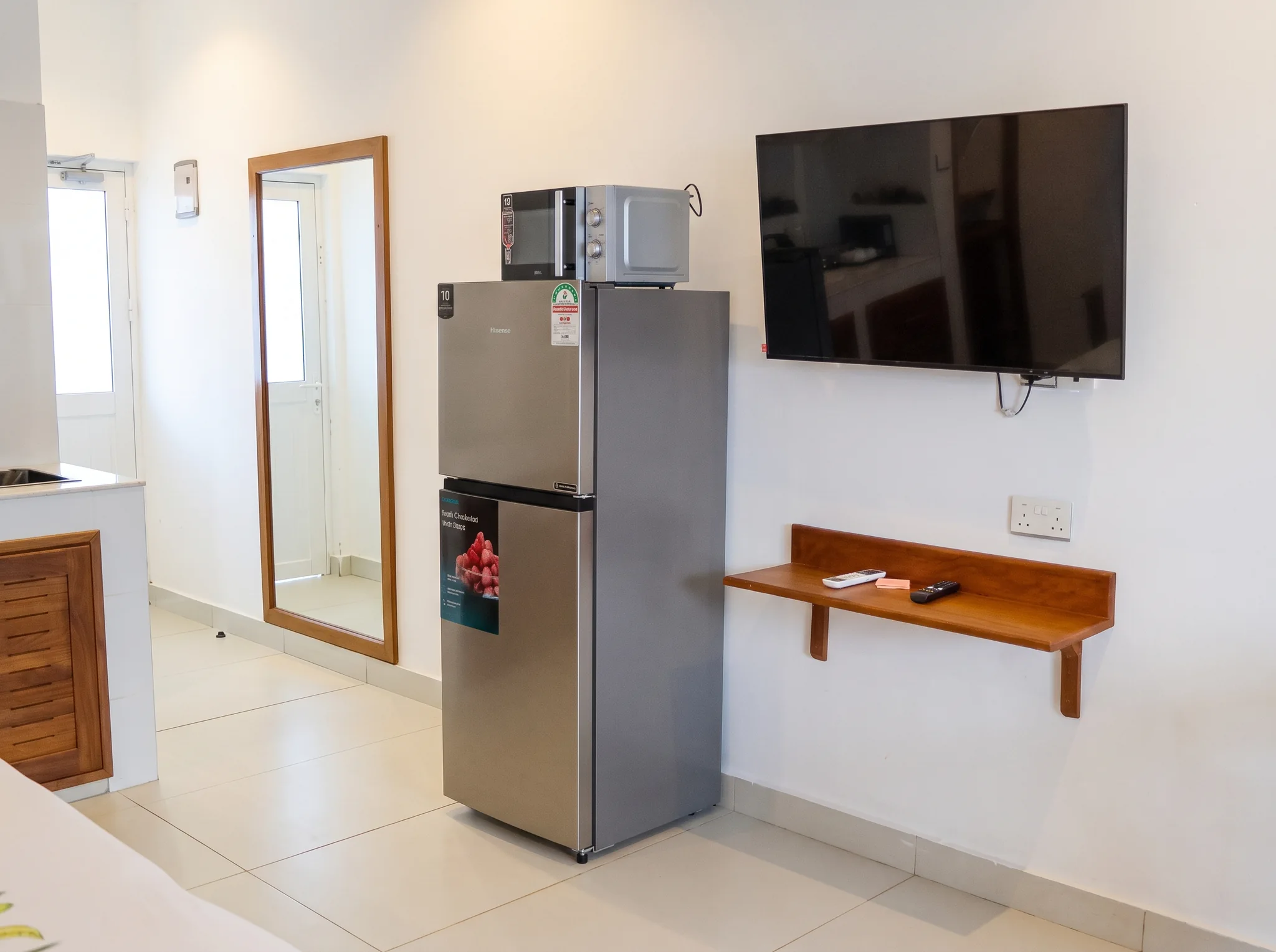 Deluxe studio room interior with wall-mounted TV, refrigerator, microwave, and custom hardwood cabinetry at Diani Darling